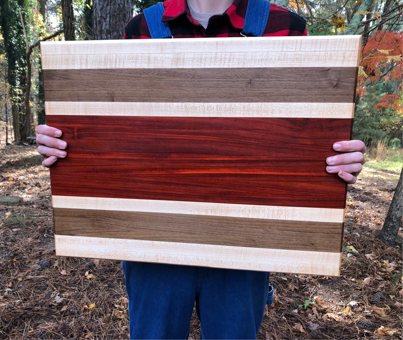 Person holding a wooden board with a striped pattern in a forest setting